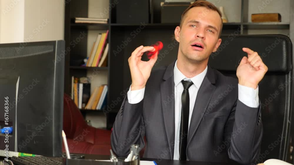 Red hand spinner, or fidgeting spinner, rotating on man's hand. Man in a suit spinning a fidget spinner in his office at his desk. Twists on the nose. 4k. Slow motion