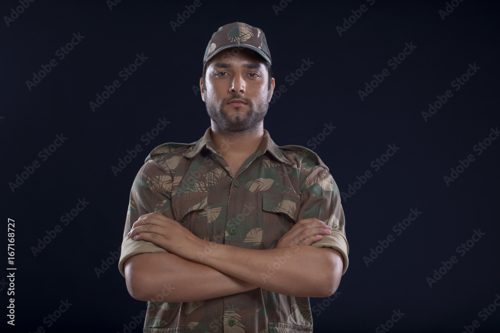 Fototapeta premium Portrait of a soldier standing with his arms crossed over blue background 