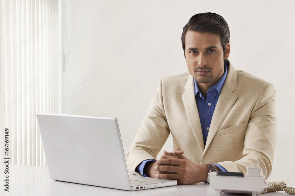 Portrait of confident businessman with laptop and landline at office desk Portrait of confident businessman with laptop and landline at office desk