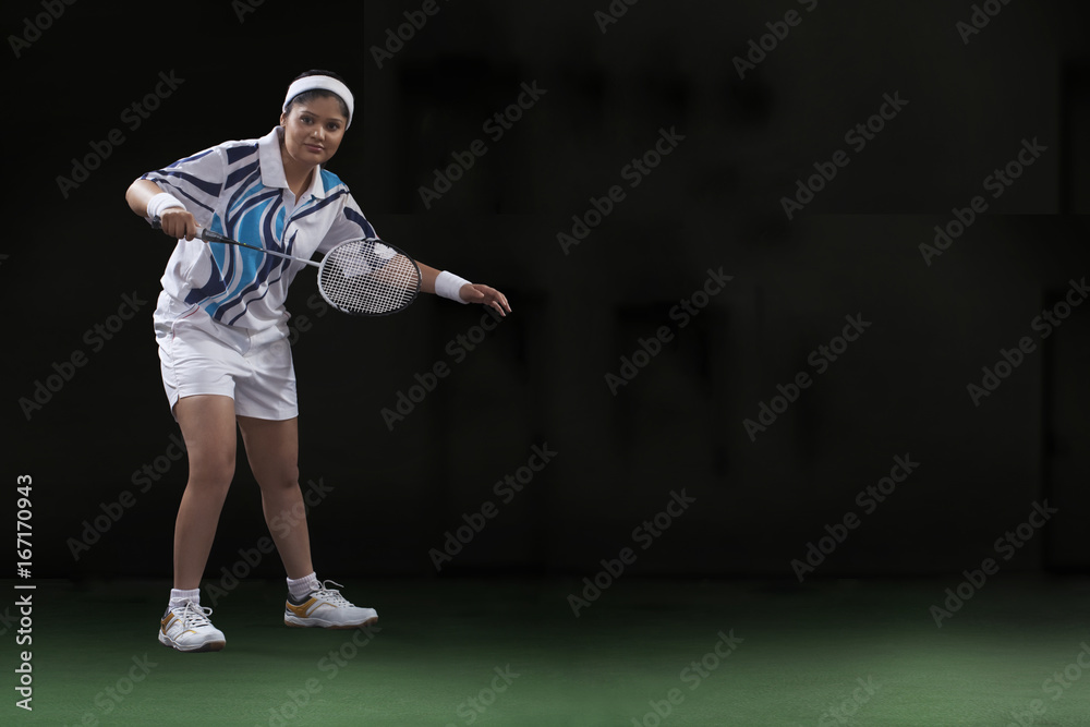Full length portrait of young woman playing badminton isolated over black background