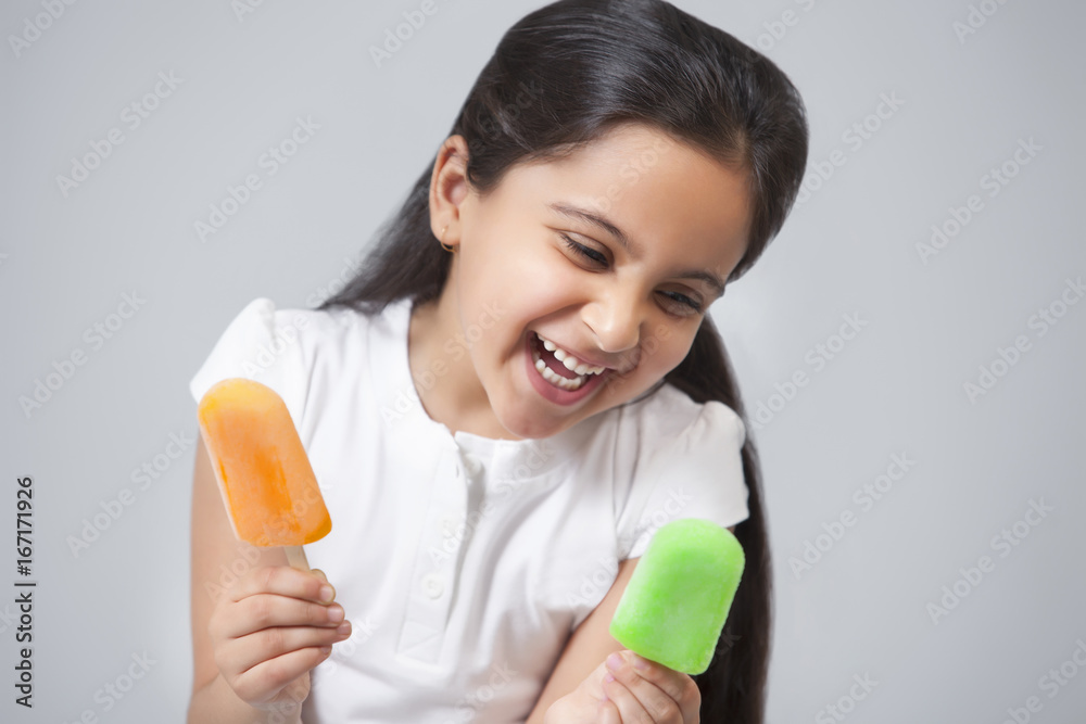 Happy little girl looking at ice lollies isolated over gray background Happy little girl looking at ice lollies isolated over gray background
