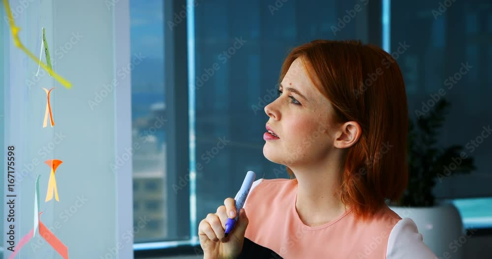 Female executive writing over sticky note on glass board