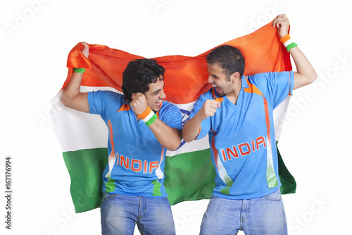 Photography Excited young male friends in jerseys cheering while holding Indian flag over wh