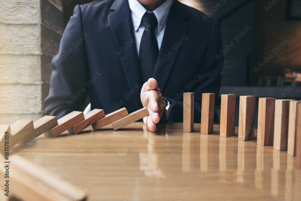 © Freedomz - Close up of businessman hand Stopping Falling wooden Dominoes effect from continuous toppled or risk, strategy and successful intervention concept for business