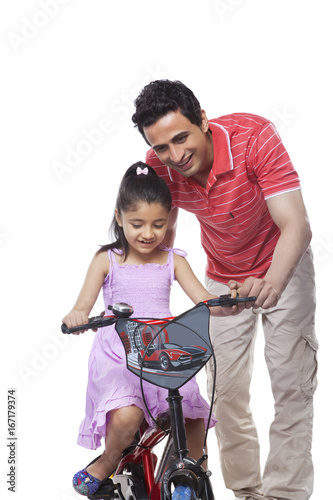 Father teaching daughter to ride bicycle over white background