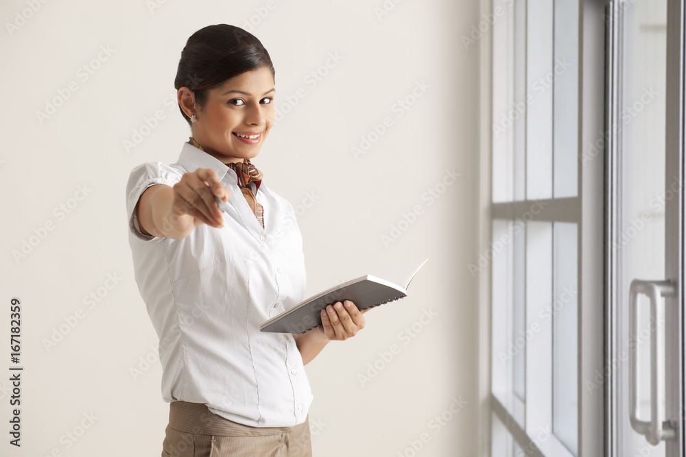 Portrait of young female executive giving pen to write in diary Portrait of young female executive giving pen to write in diary
