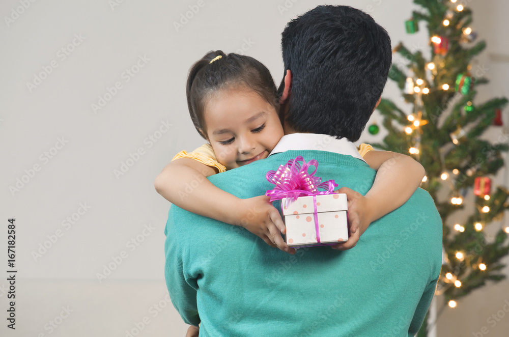 Smiling young girl hugging her dad while holding Christmas gift Smiling young girl hugging her dad while holding Christmas gift