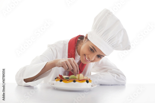 Obraz na plátně Female chef making mixed fruit cake isolated over white background