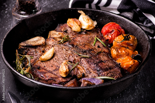 Фотография Pan grilled large t-bone steak with garlic, tomatoes, herbs and seasoning