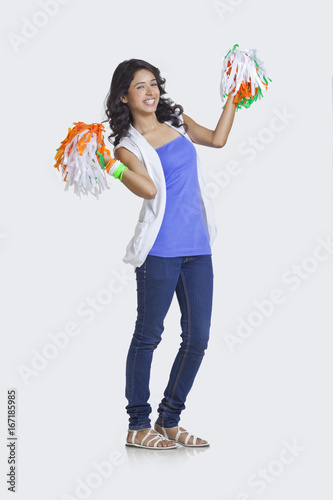 Sticker Full length portrait of young woman in casuals holding Indian tricolor pom poms