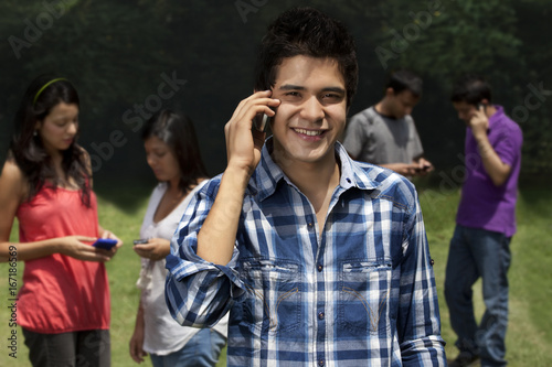 Portrait of young man using phone with friends in the background  © IndiaPix