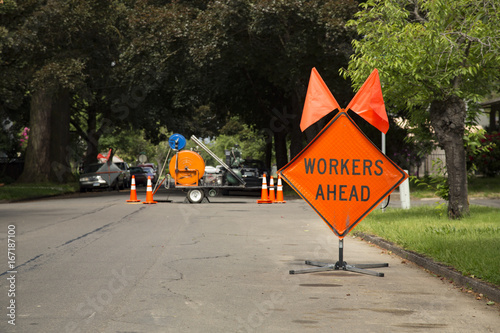 Orange and Black "Workers Ahead" Sign in Residential Neighborhood with Equipment in Background, Daytime