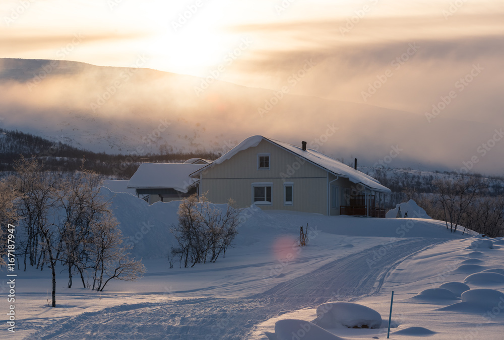 Sunrise behind mountain with house in front in frozen country in winter