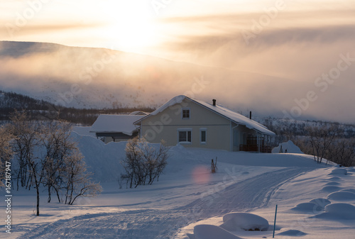 Sunrise behind mountain with house in front in frozen country in winter