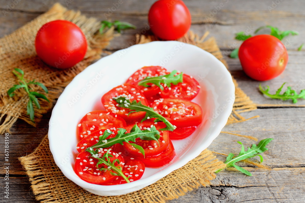 Salad with tomato, rucola, sesame seeds and vinaigrette dressing. Quick tomato salad on a white plate and an old wooden table. Healthy recipe for breakfast, lunch and dinner. Rustic style Salad with tomato, rucola, sesame seeds and vinaigrette dressing. Quick tomato salad on a white plate and an old wooden table. Healthy recipe for breakfast, lunch and dinner. Rustic style