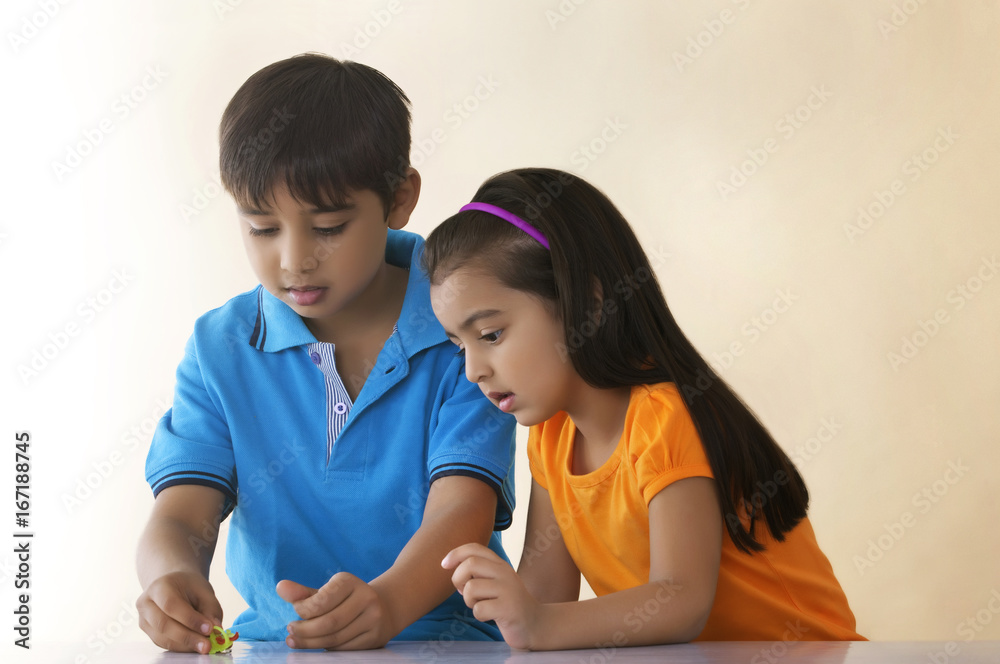 Brother and sister playing with toy at table over colored background