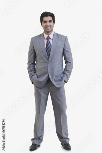 Full length portrait of happy young businessman with hands in pockets standing against white background 