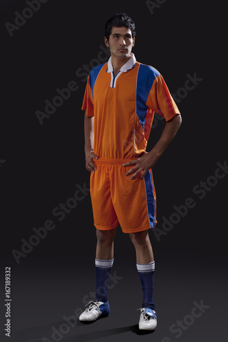 Full length of soccer player standing with hands on hip as he looks away isolated over black background