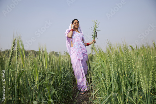 Fototapeta Naklejka Na Ścianę i Meble -  Low angle view of Indian female farm worker talking on mobile phone 