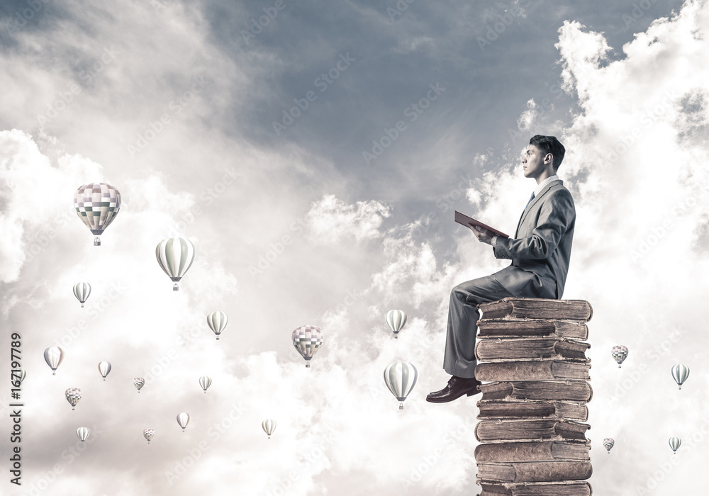 Man student reading book and aerostats flying around in air Man student reading book and aerostats flying around in air