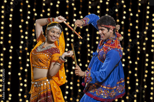 Happy young couple performing Dandiya Raas against neon lights