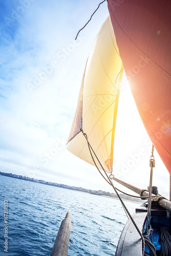 beige cotton jib sail and an ocher sail filled by the wind with wooden mast, bowsprit and hull of an old rigging sailing boat during a sunny sea trip in brittany © ydumortier