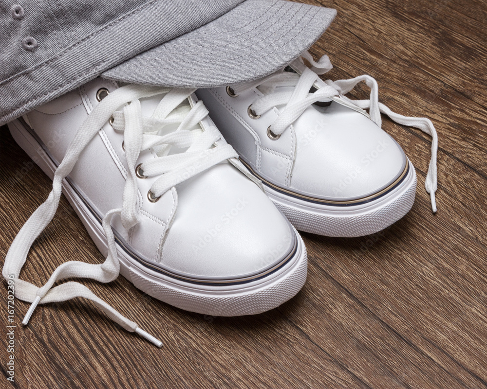 White sneakers with gray cap on dark wooden surface White sneakers with gray cap on dark wooden surface