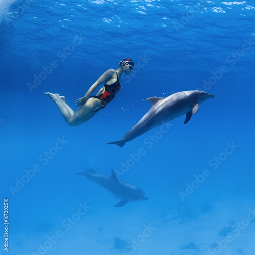 Good relationship with wild animals. Professional swimmer girl in sport swimsuit and friendly dolphins playing in deep blue sea underwater © willyam