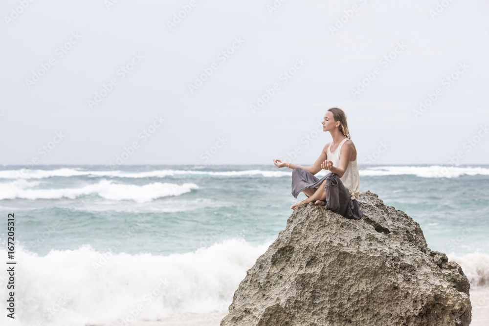 Girl sit at the seaside on the rock and meditating in yoga woman pose