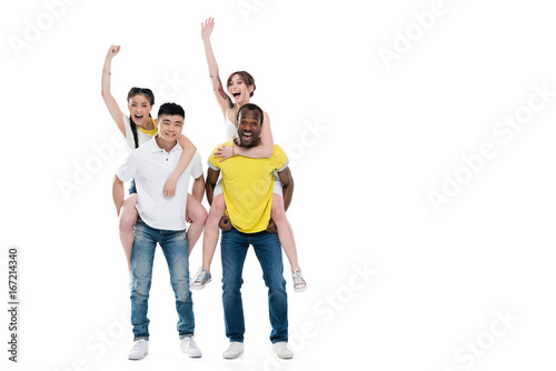 young multiethnic men piggybacking beautiful smiling girls isolated on white