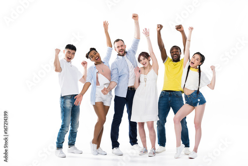 group of happy young multiethnic people triumphing and smiling at camera isolated on white