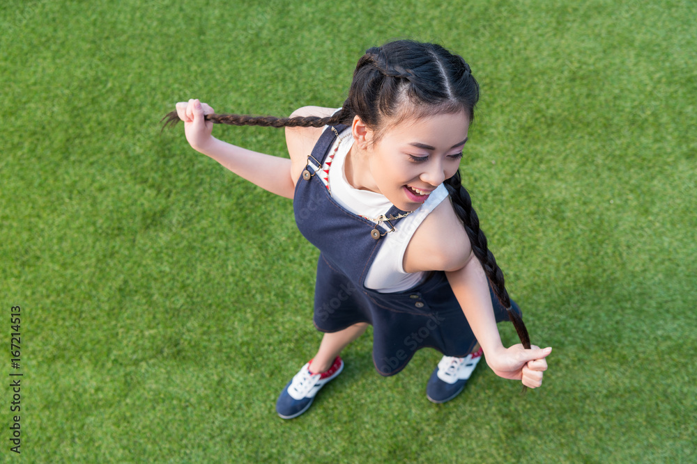 high angle view of beautiful smiling asian girl posing while standing on green grass high angle view of beautiful smiling asian girl posing while standing on green grass
