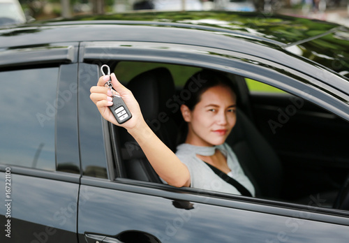 Portrait of a young asian woman inside a car, hold the key out from the window. Focus at a key hanging at her hand.