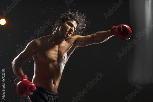 Boxer hitting punching bag over black background 