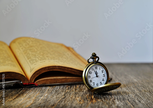 A pocket watch and an old book on a wooden background
