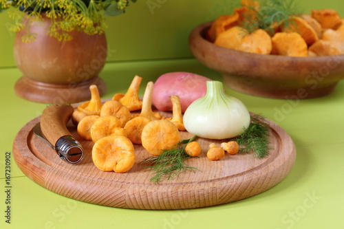 Fresh chanterelles and vegetables are on a green wooden background.