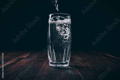 Water pours into a full faceted glass on a black background