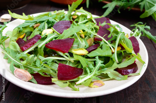 Vegan vegetable vitamin salad from beets, arugula and pistachios on a dark wooden background.