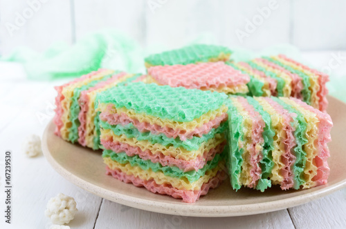 Tasty sweet colorful air waffle cake and cappuccino cup on a white wooden background.