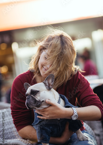 Beautiful young woman sitting in cafe restaurant and holding adorable fawn french bulldog. People and dogs theme.