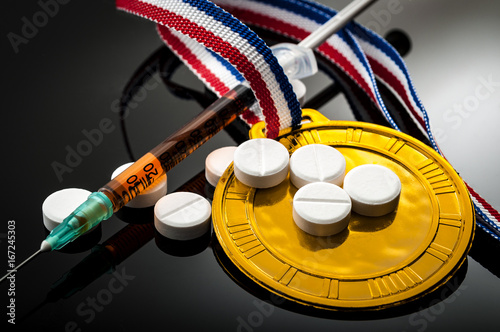 Doping in sports and steroid abuse concept with a gold medal, prescription pills and a syringe on a dark background