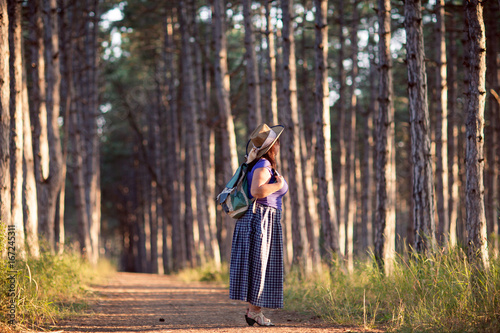 Happy senior woman in a straw hat with backpack walking through the forest. Nature outdoor activity. Healthy lifestyle concept. © ekaterina1922