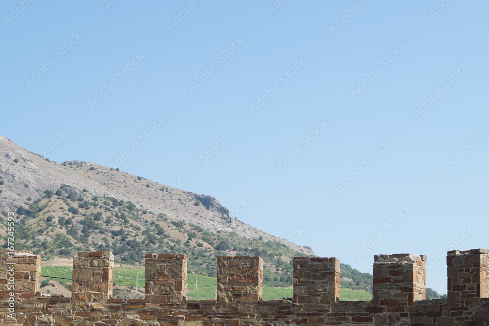Old wall with battlement in Sudak fortress, Crimea. Mountain on the background.