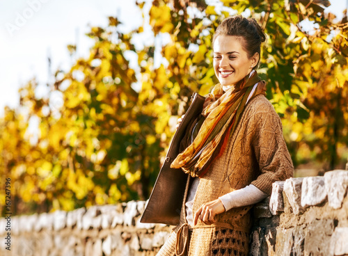 Smiling woman in comfortable clothing is standing in autumn park