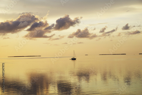  A serene and lonely sailboat in the middle of the ocean after sunset with beautiful clouds reflecting int he water.