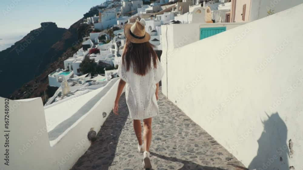 Young sexy woman is on the greek island Santorini in a white dress and and straw hat white greek houses volcano sea sunny weather