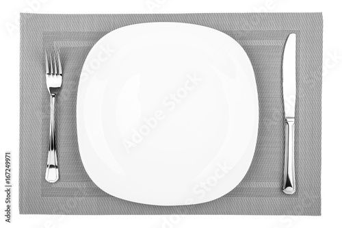 Fork, table knife and empty white plate on a placemat closeup, top view