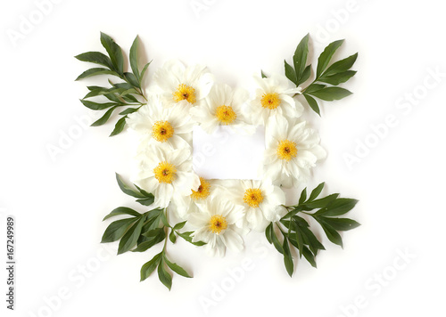 Blank paper with heart-shaped floral frame made of white peony flowers and big green leaves. Top view, flat lay.