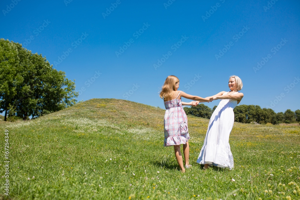 Mother and daughter dancing in a meadow. Young mom and her little daughter holding hands spinnig together. Mother and daughter dancing in a meadow. Young mom and her little daughter holding hands spinnig together.