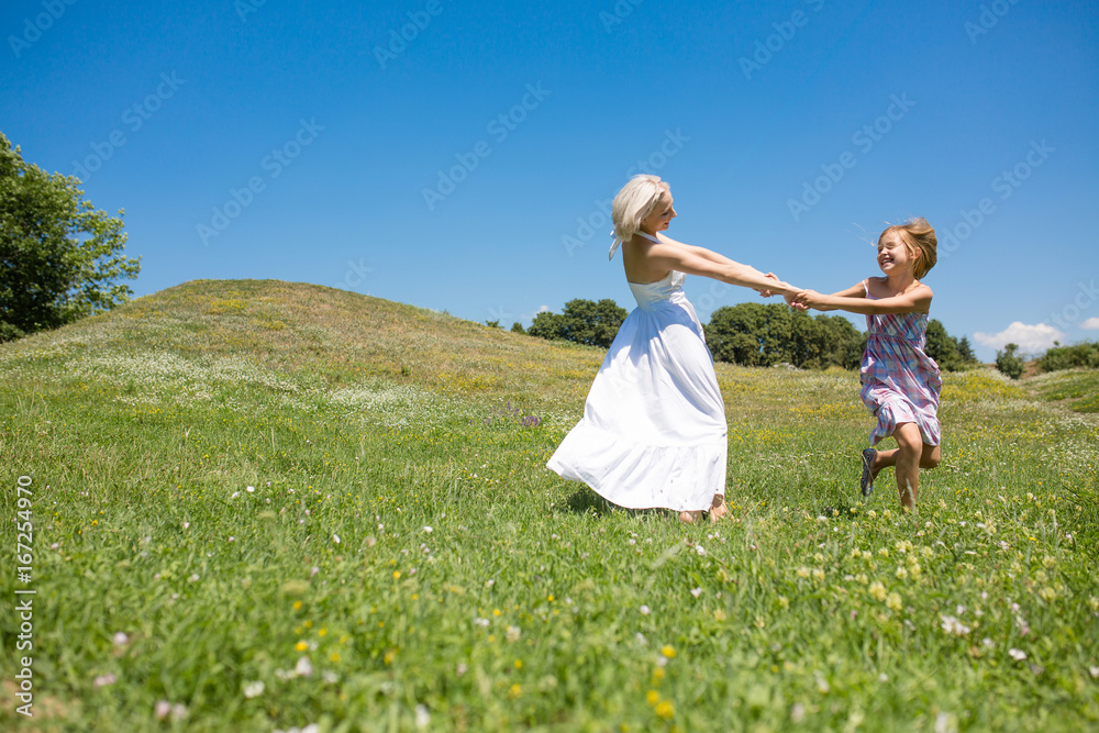 Mother and daughter holding hands, spinning, smiling. Happy woman with her child having fun in a meadow. Mother and daughter holding hands, spinning, smiling. Happy woman with her child having fun in a meadow.